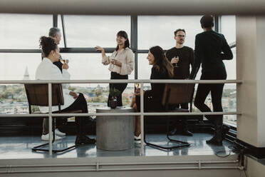 Lächelnde männliche und weibliche Kollegen trinken Wein beim Feiern auf einer Büroparty - MASF22407