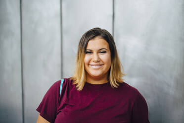 Portrait of smiling female student against gray wall - MASF22442