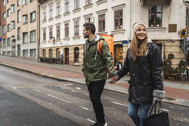 Lächelndes Paar hält sich beim Überqueren der Straße in der Stadt an den Händen - MASF22470
