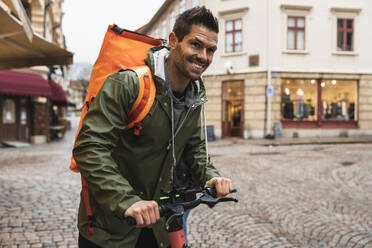 Lächelnder Mann mit Elektro-Scooter auf der Straße in der Stadt - MASF22474