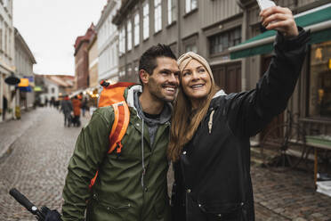 Lächelndes heterosexuelles Paar macht Selfie auf der Straße in der Stadt - MASF22477