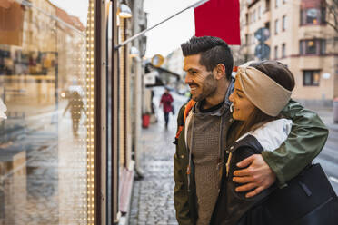 Smiling man arm around woman while doing window shopping in city - MASF22485