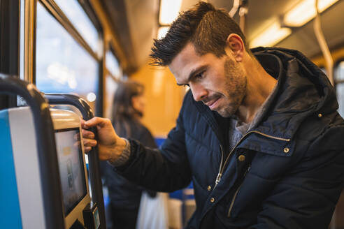 Lächelnder Mann, der eine Fahrkarte kauft, während er mit der Straßenbahn fährt - MASF22503