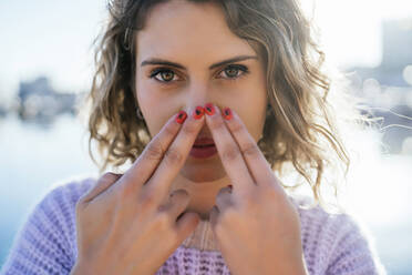 Beautiful woman keeping fingers on nose against sky - MPPF01557