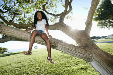 Young mixed race girl sitting in a tree branch - MINF15931