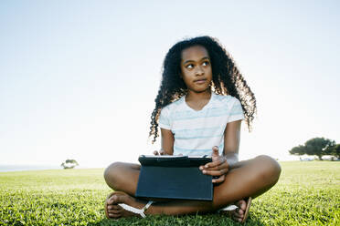 Nine year old mixed race girl outdoors with a digital tablet. - MINF15937