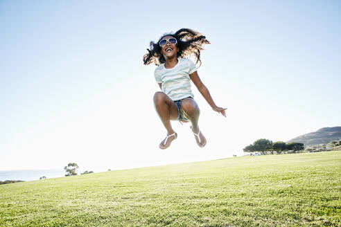 Junges gemischtrassiges Mädchen mit langen lockigen Haaren springt in die Luft - MINF15950