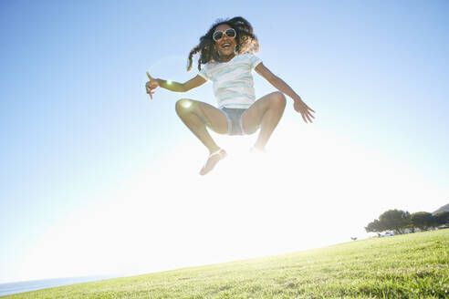 Junges gemischtrassiges Mädchen mit langen lockigen Haaren springt in die Luft - MINF15951