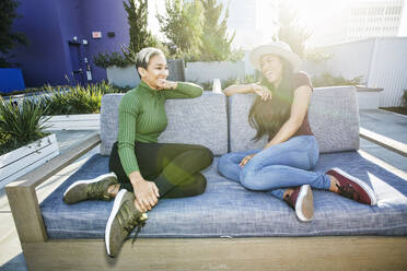 Zwei junge Frauen auf einem Sofa in einer Dachterrasse in der Abenddämmerung - MINF16077
