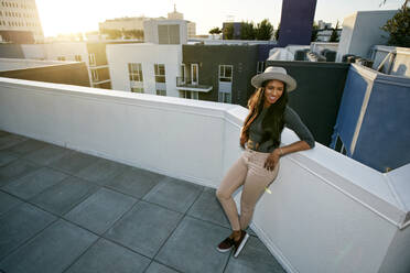 Young woman leaning on a parapet at sunset, city buildings in the background. - MINF16096