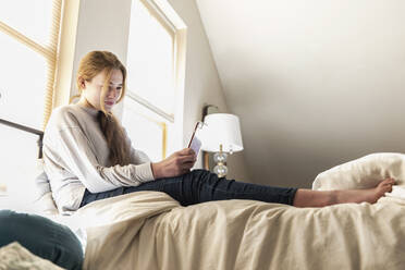 Teenager-Mädchen liegt im Bett und benutzt ihr Smartphone - MINF16114
