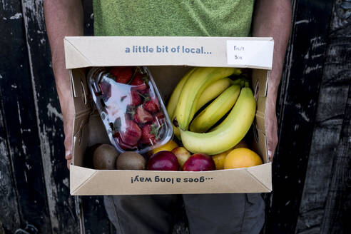 Close up of person holding an organic fruit and vegetable box with a selection of fresh produce. - MINF16139