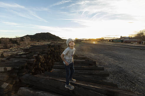 7 year old boy standing alone on railroad ties at sunset - MINF16167