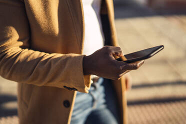 Anonymer junger Afroamerikaner in trendigem Outfit auf der Straße, der an einem sonnigen Sommertag auf seinem Mobiltelefon surft - ADSF21120