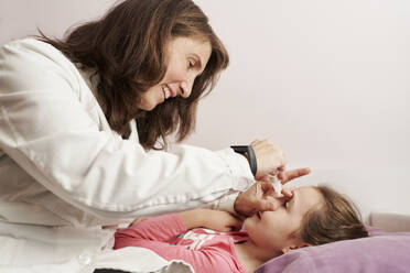 Eine Ärztin lächelt und gibt einem kleinen Mädchen in ihrem Bett Augentropfen. Hausarztkonzept - CAVF93644
