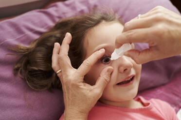Detail einer lächelnden Ärztin, die einem kleinen Mädchen in ihrem Bett Augentropfen verabreicht. Hausarztkonzept - CAVF93645