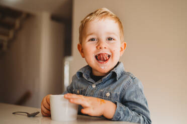 Liebenswerter weißer Junge mit Milchschnurrbart lächelnd mit herausgestreckter Zunge - CAVF93652
