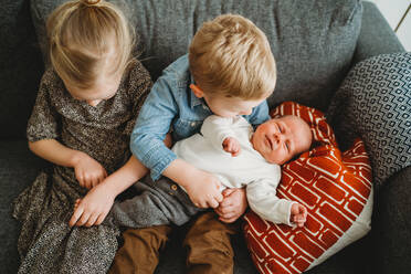 Baby auf der Couch zu Hause mit Bruder und Schwester halten ihn - CAVF93654