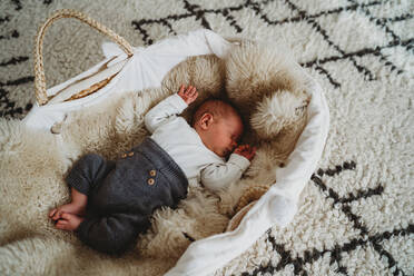 Adorable white newborn baby sleeping in Moses basket with cozy rug - CAVF93659