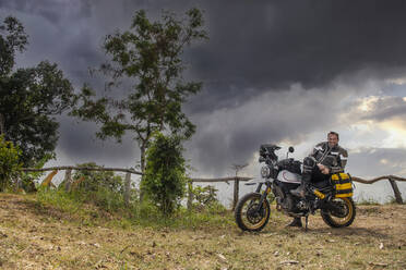 Ein Mann posiert auf seinem Geländemotorrad vom Typ Scrambler in Thailand - CAVF93663