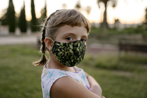 Girl with bangs and protective face mask staring while standing at park - AMPF00109