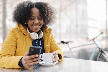 Lächelnde Frau mit Kaffeetasse und Smartphone in einem Straßencafé - JCZF00501