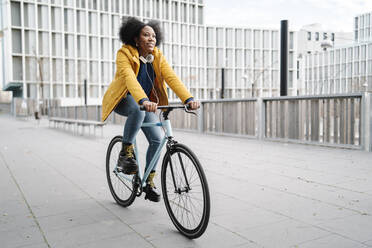 Young woman riding bicycle on footpath against building - JCZF00508