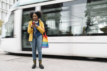 Junge Frau schreibt SMS auf ihrem Handy, während sie auf dem Fußweg vor der Straßenbahn steht - JCZF00518