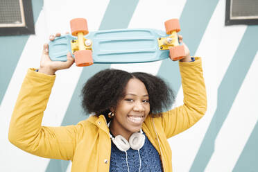 Lächelnde Frau hält Skateboard gegen die Wand - JCZF00529