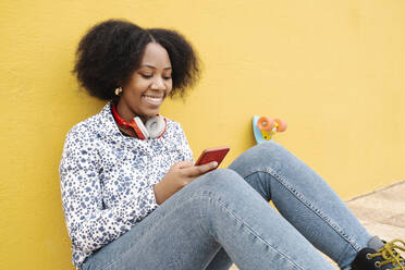 Smiling woman text messaging through mobile phone on footpath against wall - JCZF00532