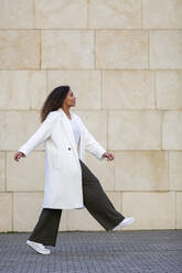 Young woman walking on footpath by wall - MTBF00901