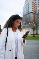 Junge Frau, die im Park eine SMS auf ihrem Smartphone schreibt - MTBF00903