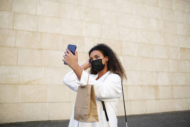 Junge Frau, die ein Selfie mit ihrem Smartphone auf dem Fußweg vor einer Mauer macht - MTBF00905