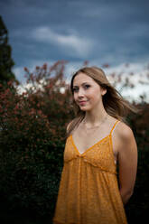 A young woman in a dress stands among flowering shrubs with the Blue Ridge Mountains in the background - CAVF93708