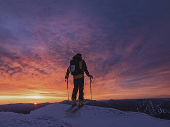 Skier silhouetted against red sunrise on mountain peak, New Hampshire - CAVF93714