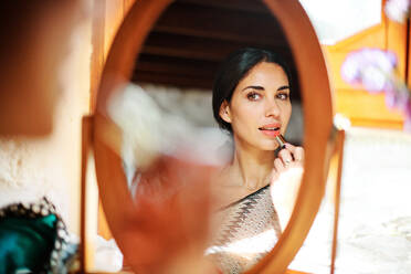 Crop junge sanfte weibliche Make-up Lippen mit Lippenstift beim Blick in den Spiegel im Sonnenlicht - ADSF21137