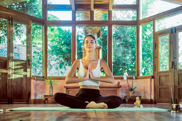 Junge konzentrierte Frau mit geschlossenen Augen praktiziert Yoga mit gekreuzten Beinen in der Nähe der Schale Gong im Haus - ADSF21147