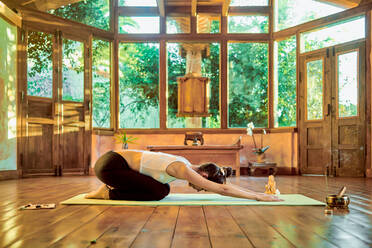 Side view of flexible woman sitting in Baddha Konasana pose while practicing yoga on floor in sunlight - ADSF21148