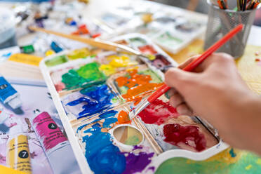 Crop anonymous painter mixing paints with brush using watercolor palette while working in art studio - ADSF21192