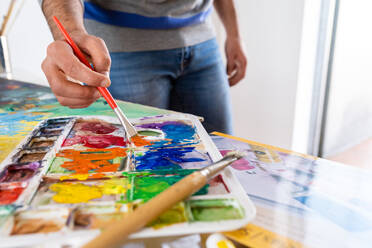 Anonymer männlicher Maler beim Mischen von Farben mit einem Pinsel und einer Aquarellpalette während der Arbeit im Kunststudio - ADSF21193