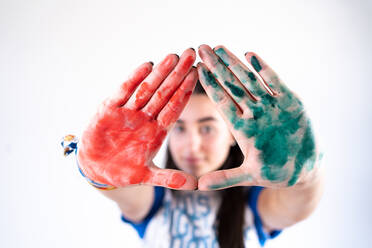 Young female artist looking at camera with stretched arms with red and green paints on palms of hands - ADSF21201