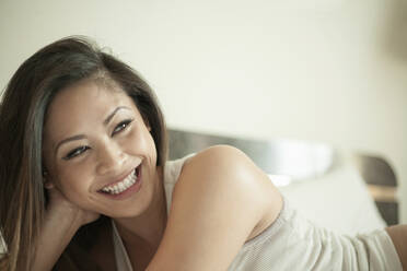 Lächelnde Frau, die wegschaut, während sie zu Hause auf dem Bett liegt - AJOF01260