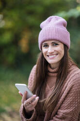 Lächelnde Frau mit Mobiltelefon im Garten - AKLF00128