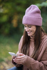 Lächelnde Frau, die ein Mobiltelefon benutzt, während sie im Garten sitzt - AKLF00129