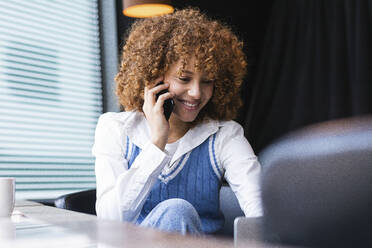 Teenage girl smiling while talking on mobile phone at cafe - PNAF00919