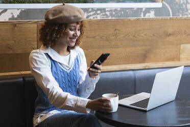 Weiblicher Teenager, der in einem Café Kaffee trinkt und dabei sein Handy benutzt - PNAF00924