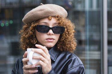 Female teenager wearing beret and sunglasses having coffee outdoors - PNAF00926