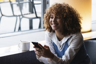 Smiling female teenager with mobile phone sitting at cafe - PNAF00938