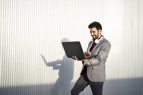 Smiling businessman using laptop in front of wall - RCPF00813