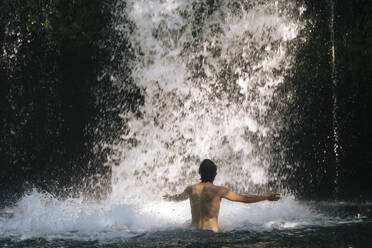 Indonesien, Bali, Mann beim Baden im Wasserfall - KNTF06177